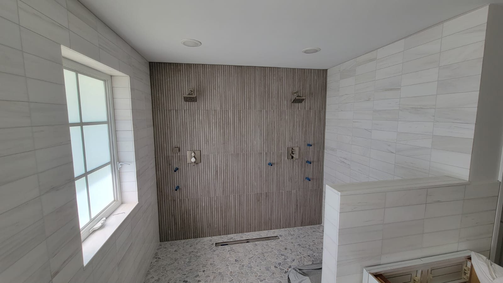 Double shower with a fluted stone feature wall, linear drain and mosaic pan