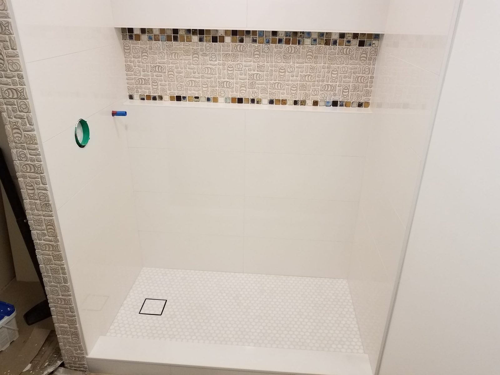 Shower wall with a glass mosaic accent band and penny-round pan, part-way through the job