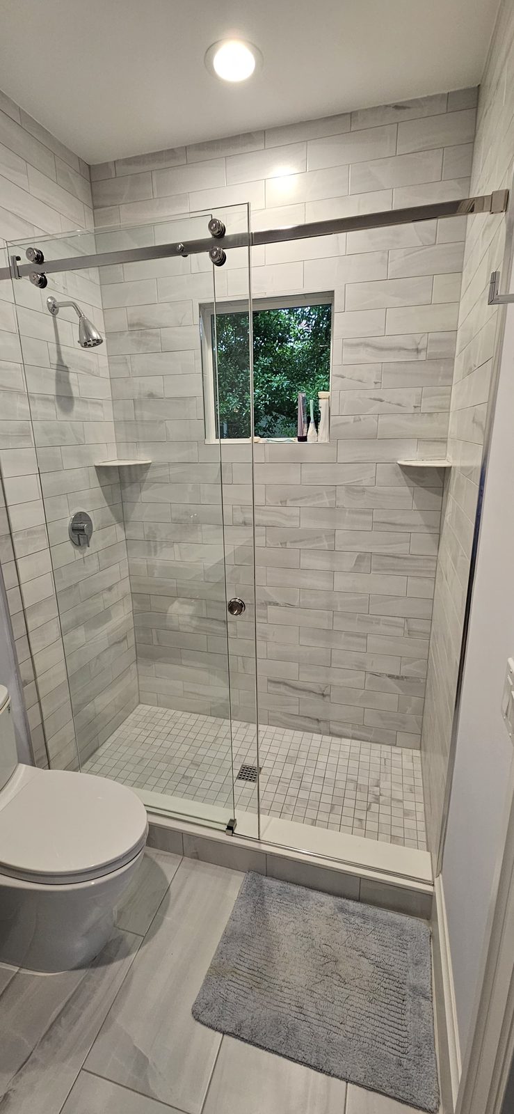 Grey-veined tile shower with a corner window and mosaic floor