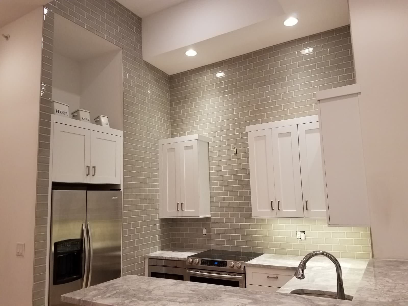 Grey glass subway backsplash taken floor to ceiling and cut around the wall cabinets