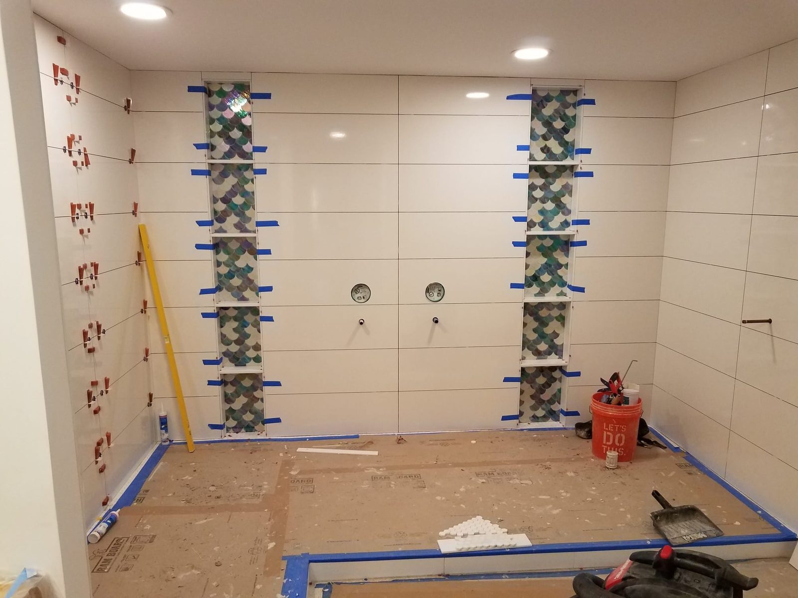 Shower walls going up — leveling clips holding the field tile while the mosaic inlays set
