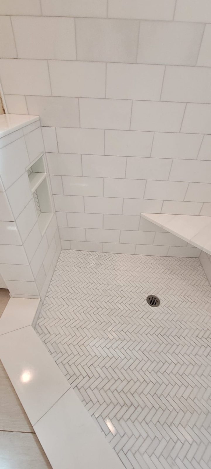 Subway tile shower with a herringbone marble pan and built-in shelf niches