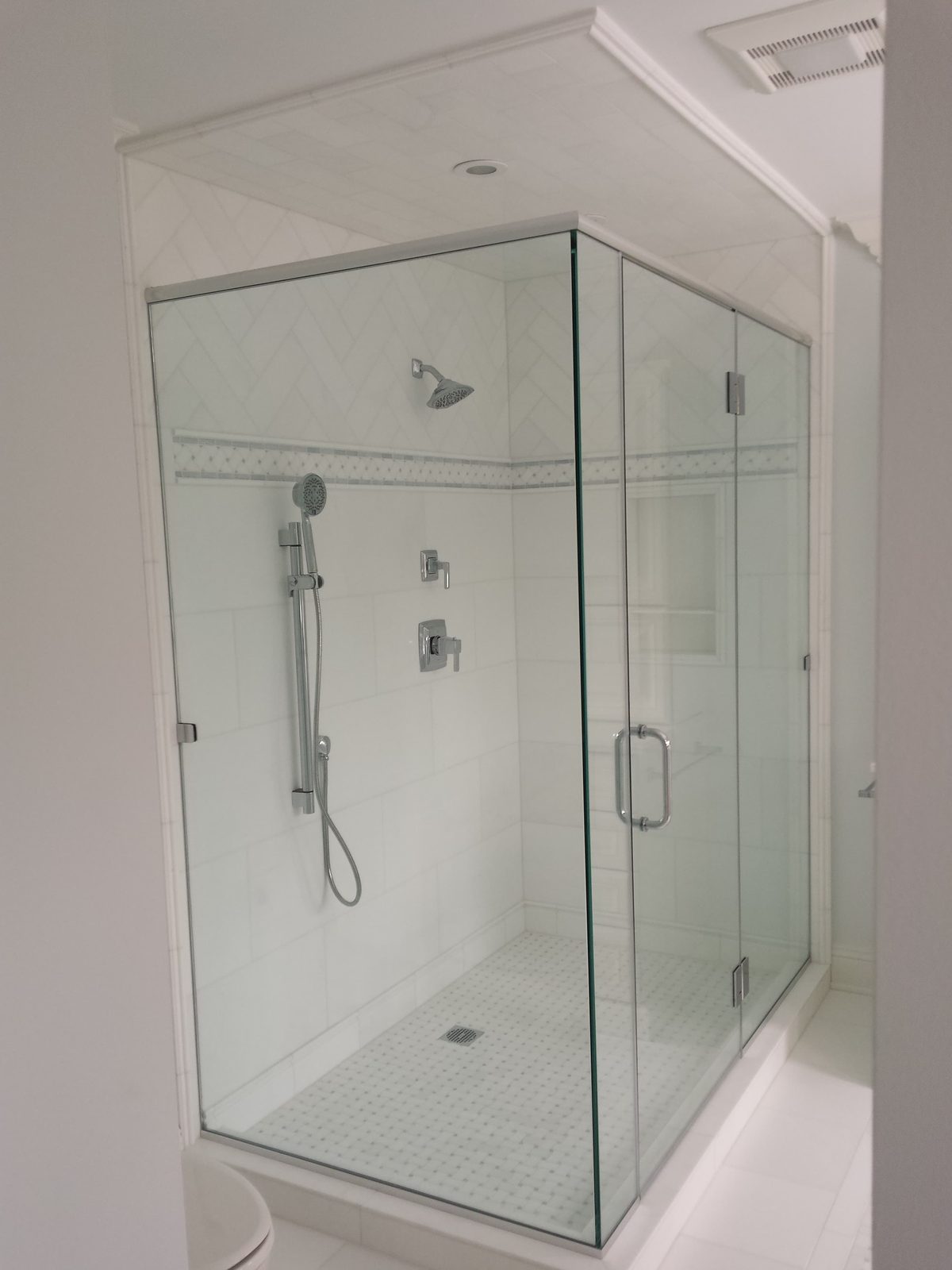 Corner shower in large-format white tile with a chevron panel and mosaic pan