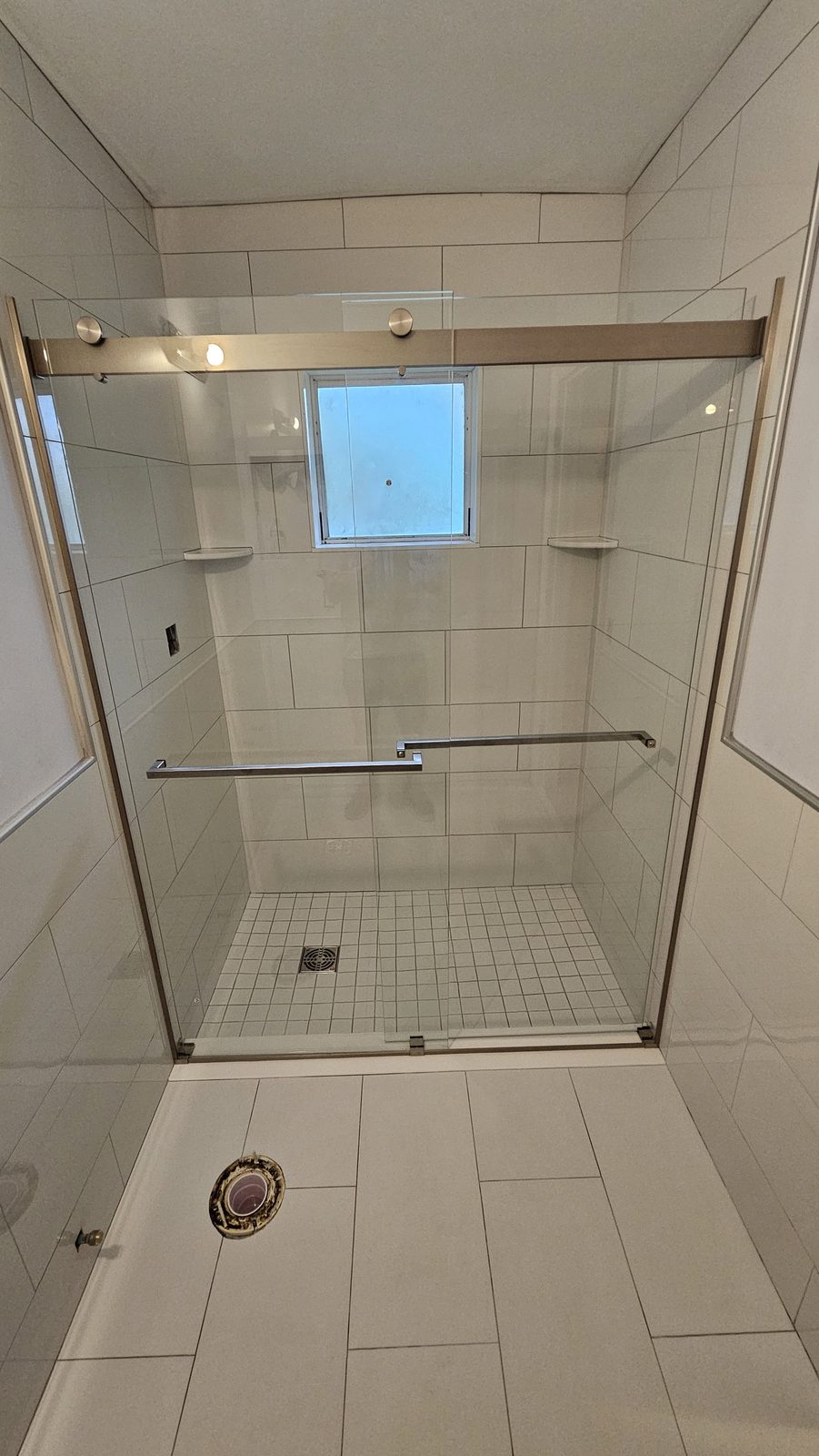 Large-format white tile shower with sliding glass doors and a mosaic pan